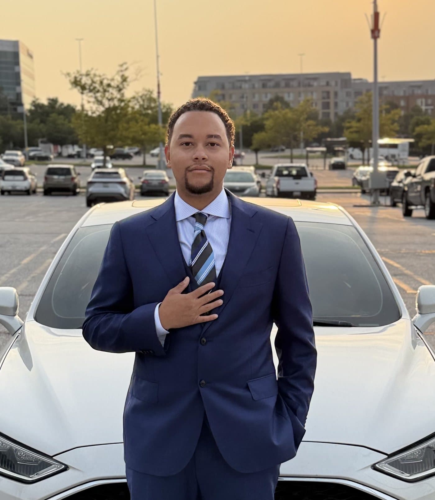 Justin Brown in a navy suit at sunset, hand on his chest